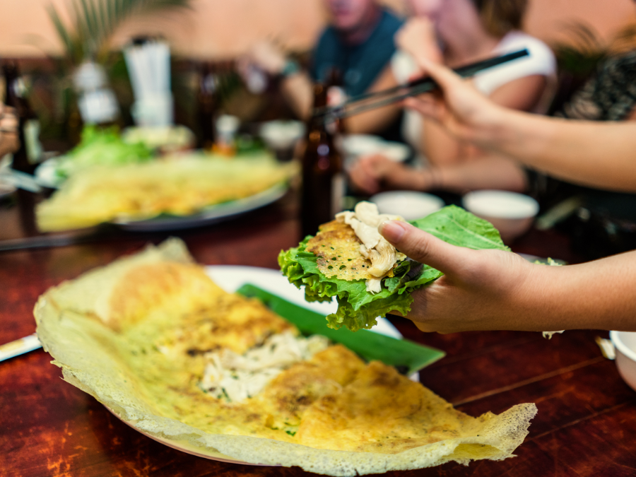 A crispy bánh xèo pancake filled with shrimp, pork, and bean sprouts, served with fresh herbs and a dipping sauce.