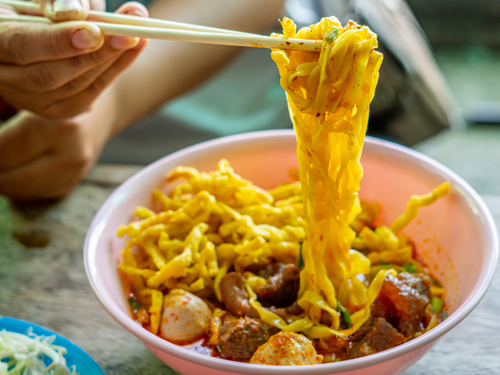A bowl of Khao Soi, Chiang Mai's famous curry noodle soup, garnished with crispy noodles and fresh lime.