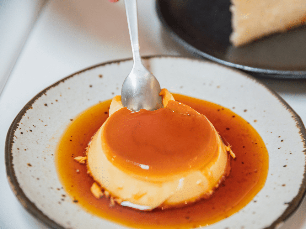 A creamy Bánh Flan topped with caramel sauce, served on a white plate.