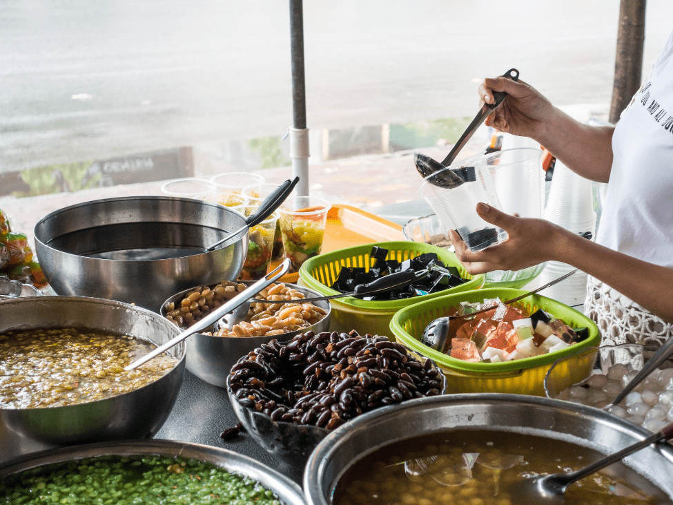 A vibrant bowl of Chè Ba Màu with layers of green jelly, red beans, and yellow mung bean paste topped with coconut milk.