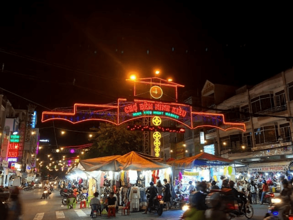 Ninh Kieu Night Market in the evening with colorful stalls.