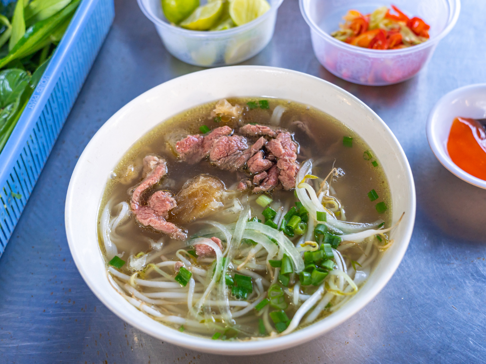 A steaming bowl of beef pho with fresh herbs and lime