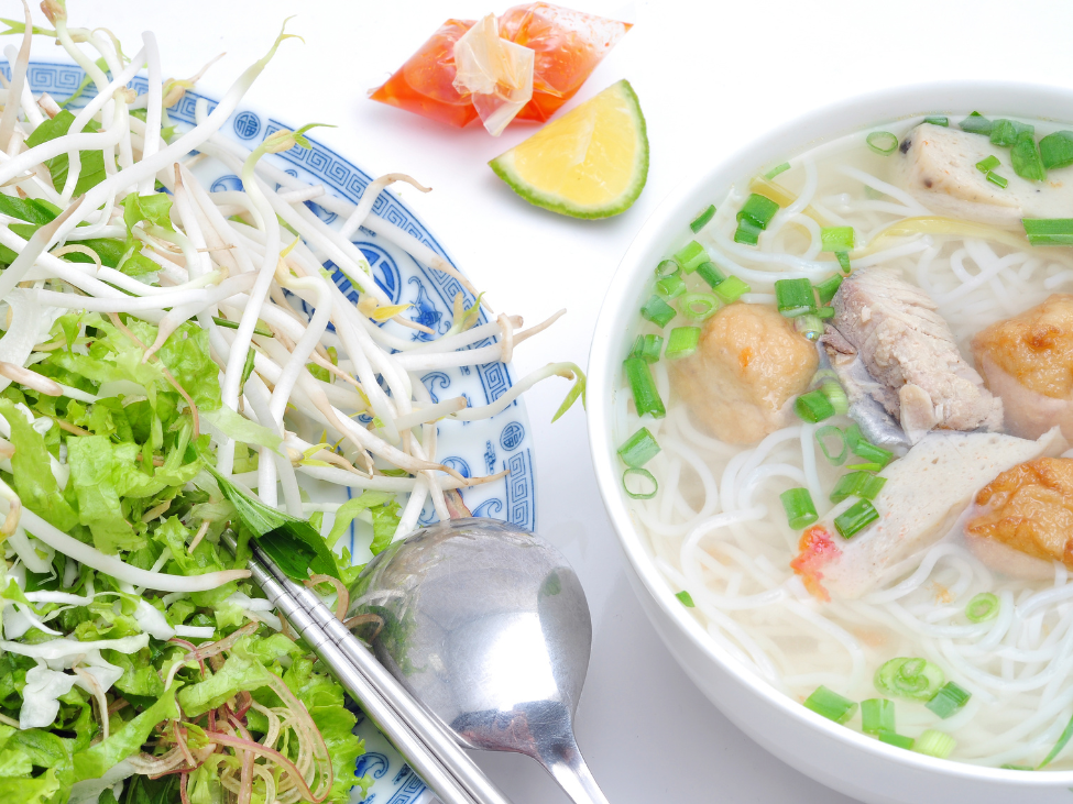 Bowl of Bun Cha Ca noodle soup with fish cakes and herbs.