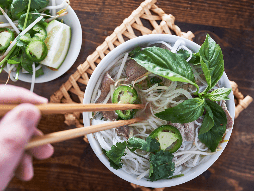 A steaming bowl of pho in Ho Chi Minh City, highlighted with fresh herbs and lime.