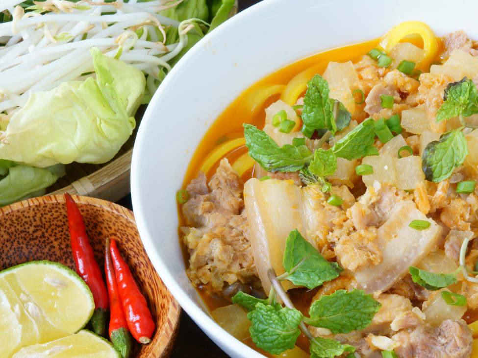 A colorful bowl of Mi Quang noodles, garnished with herbs and peanuts."