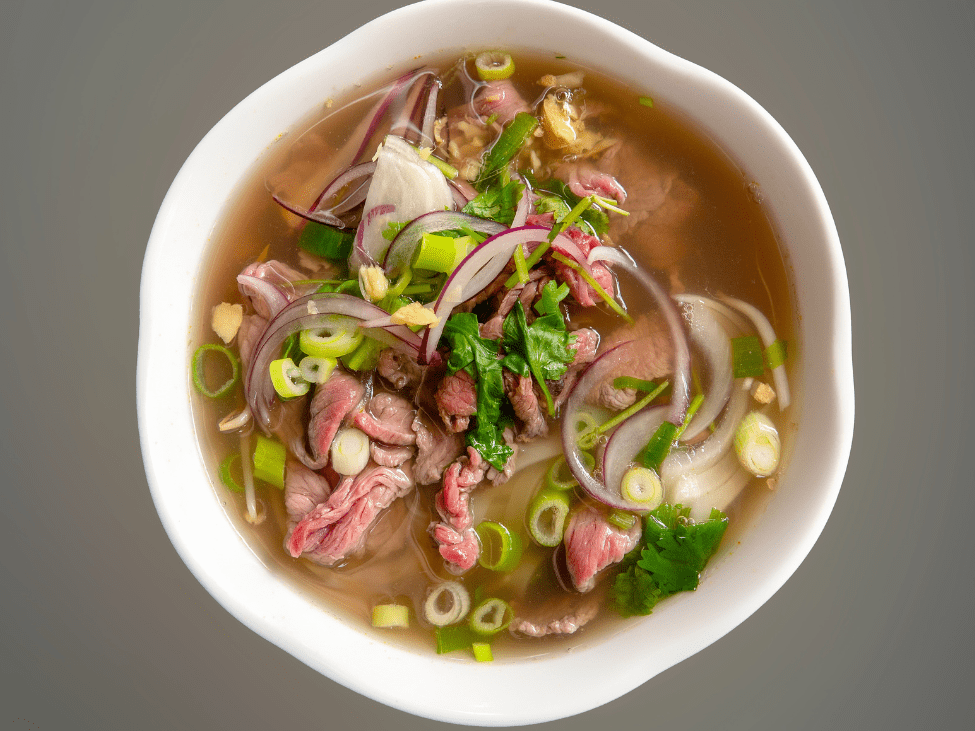 A bustling market in Da Nang featuring a bowl of pho with vibrant herbs and a clear, flavorful broth.