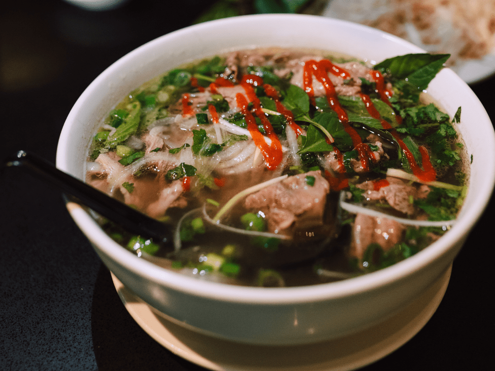 A traditional pho vendor in Hanoi's Old Quarter, serving a bowl of pho with thin-sliced beef and fresh herbs.