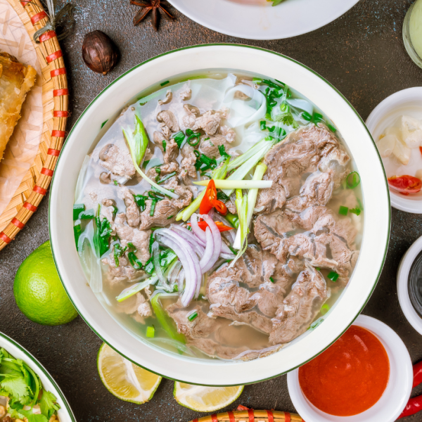 A vibrant street scene in Saigon with a steaming bowl of pho garnished with fresh herbs and beef slices.