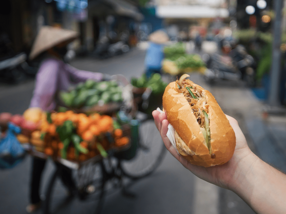 Travelers enjoying a traditional Bánh Mì sandwich in Hanoi on a Vespa food tour.