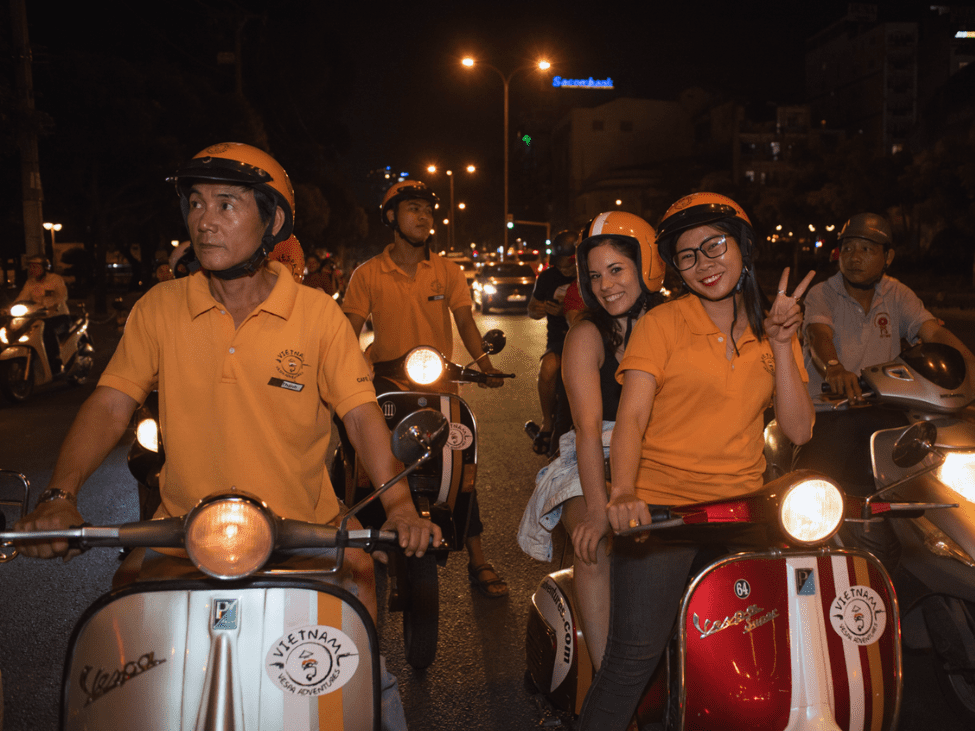 A group of people enjoying the Saigon Foodie Experience on vintage Vespas, exploring Ho Chi Minh City's culinary delights.