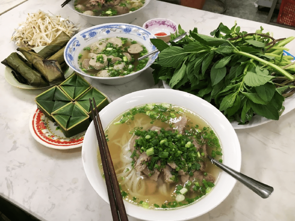 A close-up of a steaming bowl of pho at Phở Hòa Pasteur, highlighting the fresh herbs and tender beef.