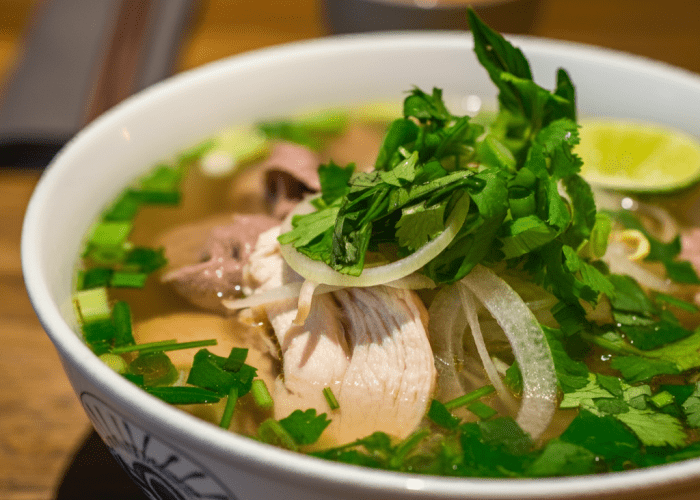 A vibrant bowl of chicken pho at Pho Soho London, served with fresh herbs and chili.