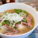 A steaming bowl of Phở Tái Lăn served at Phở Binh, featuring tender rare beef and fresh herbs.