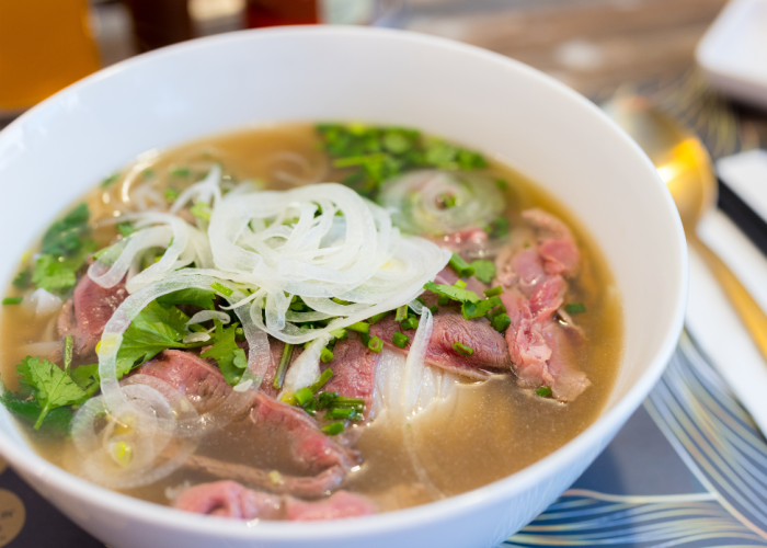 A steaming bowl of Phở Tái Lăn served at Phở Binh, featuring tender rare beef and fresh herbs.