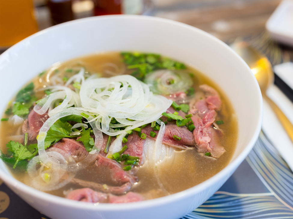 A steaming bowl of Phở Tái Lăn served at Phở Binh, featuring tender rare beef and fresh herbs.