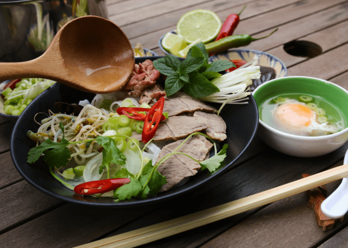 A bowl of Southern-style pho at Phở Tau Bay, garnished with fresh herbs and lime.