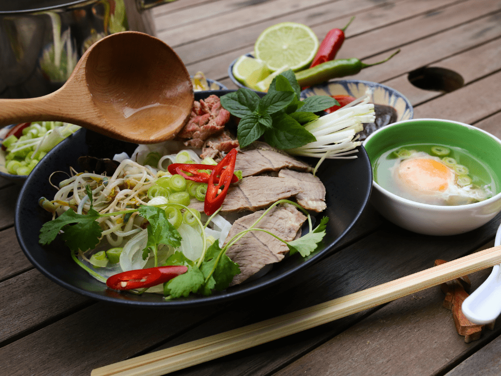 A bowl of Southern-style pho at Phở Tau Bay, garnished with fresh herbs and lime.