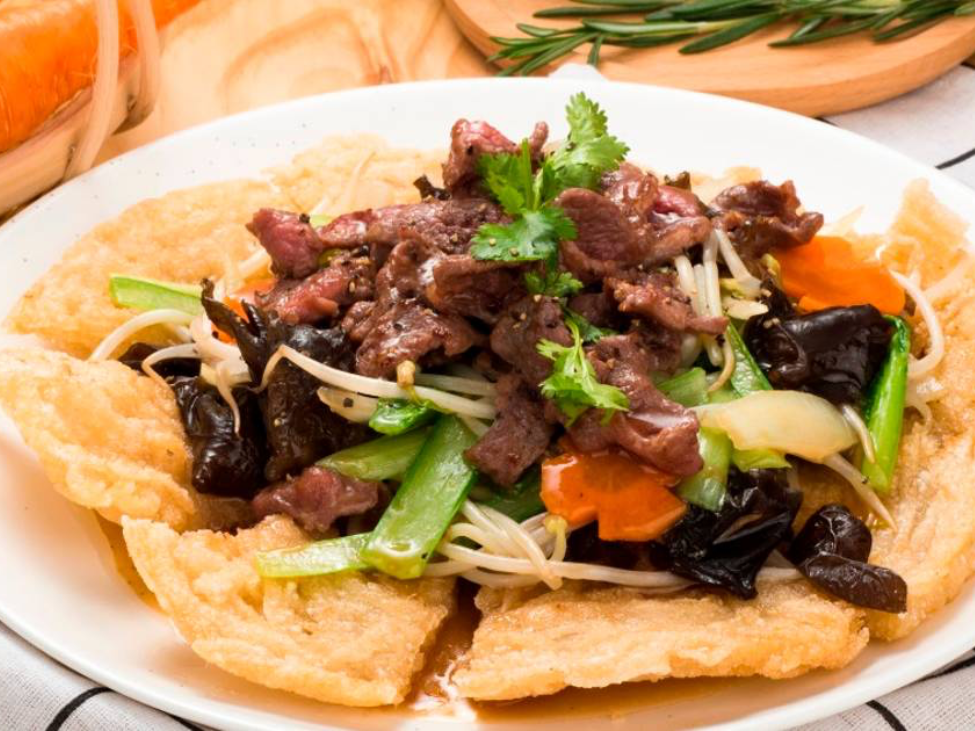 A plate of crispy Phở Áp Chảo with tender beef and fresh vegetables at Gia Truyền Bát Đàn.