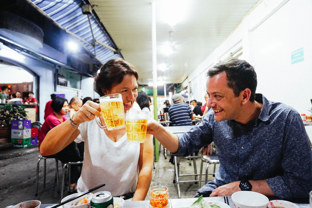 Saigon lit up at night, with couples enjoying street food from the back of a Vespa.