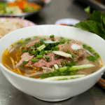 Street vendor in Hanoi preparing a fresh bowl of pho with steaming broth and herbs.