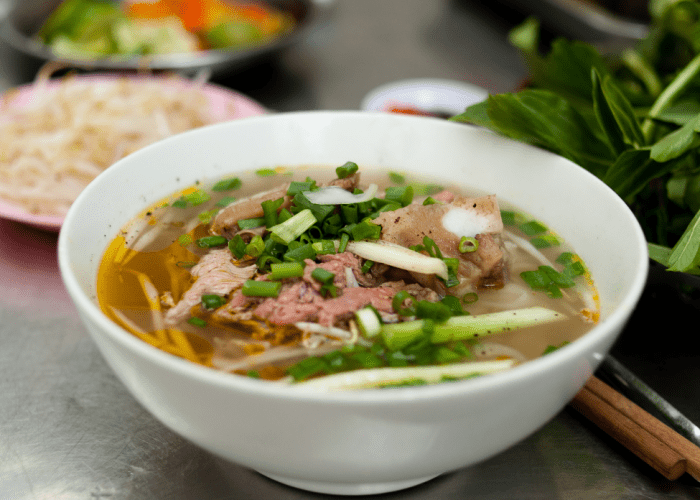 Street vendor in Hanoi preparing a fresh bowl of pho with steaming broth and herbs.