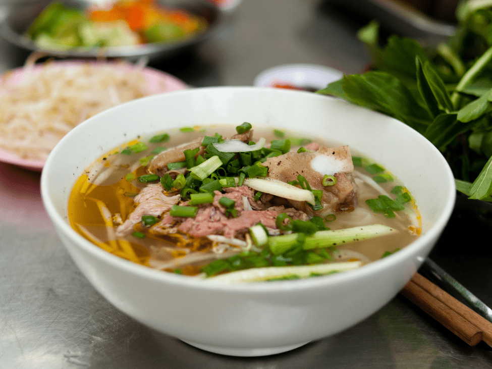 Street vendor in Hanoi preparing a fresh bowl of pho with steaming broth and herbs.