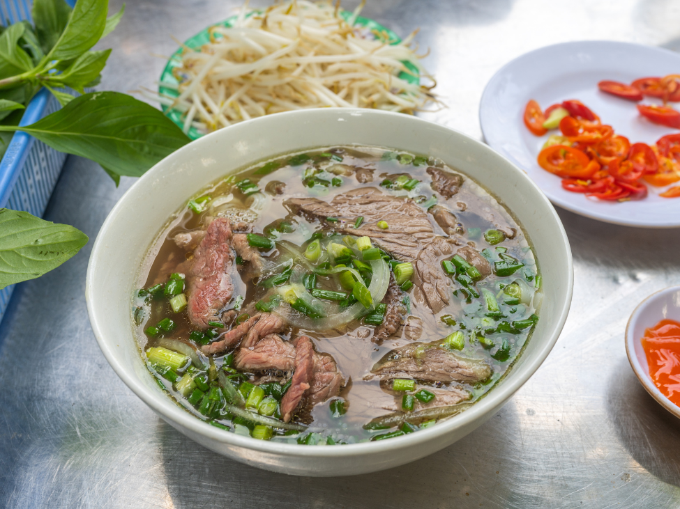 A steaming bowl of traditional pho in Hanoi with clear broth and green onions.