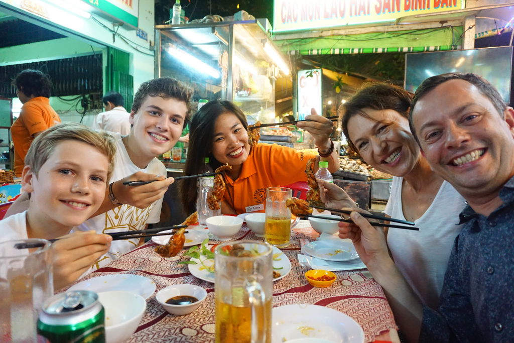 Participants on a Vespa Adventures tour exploring Saigon's street food and cultural sites at night.