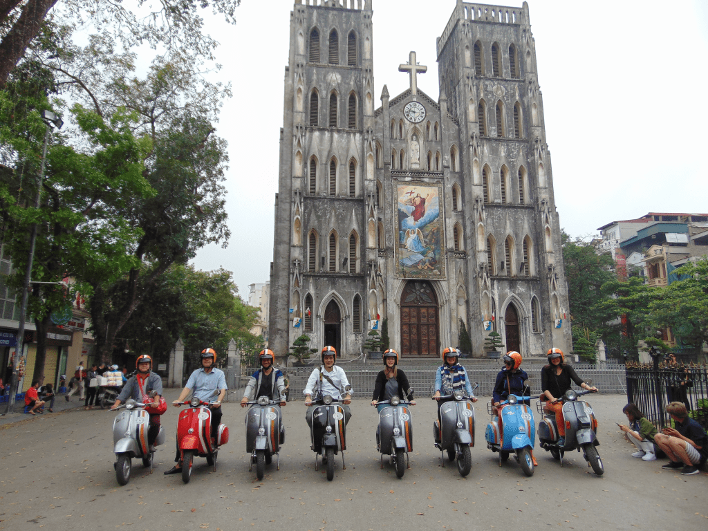 Vintage Vespa tour group enjoying street food at St. Joseph’s Cathedral in Hanoi.