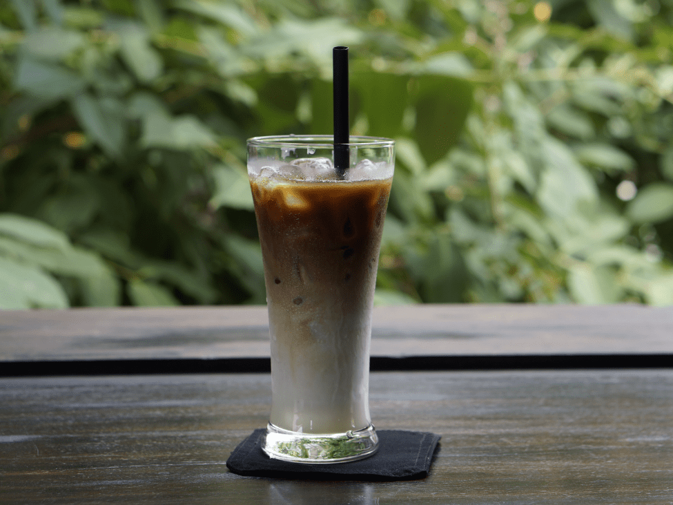 A glass of Bac Siu coffee with layers of coffee and milk, served in a transparent glass on a rustic table.