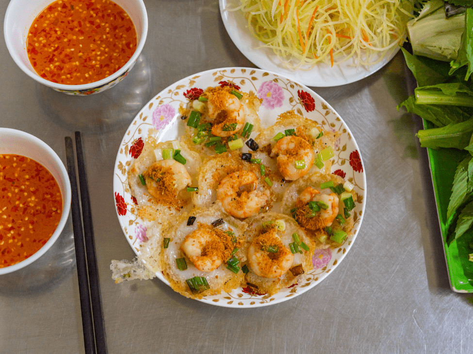 A plate of bánh khọt topped with shrimp, served with fresh herbs.