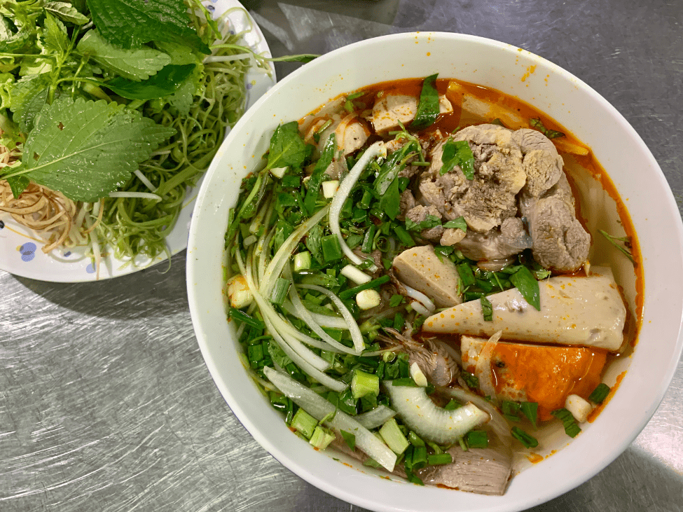 A steaming bowl of Bun Bo Hue with beef slices, herbs, and chili