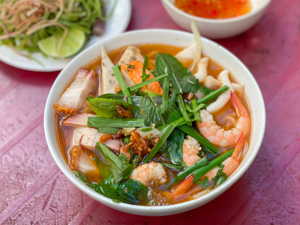 A bowl of bun mam with rice vermicelli, seafood, and pork, garnished with fresh herbs.