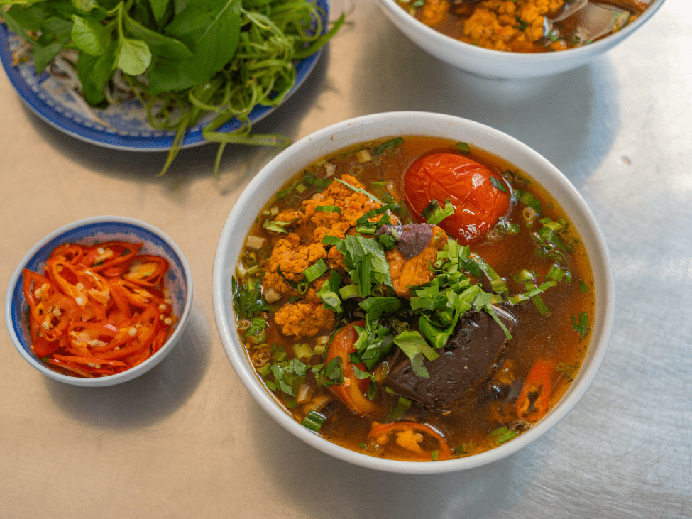 A bowl of Bun Rieu with tomatoes, crab paste, and fresh herbs.