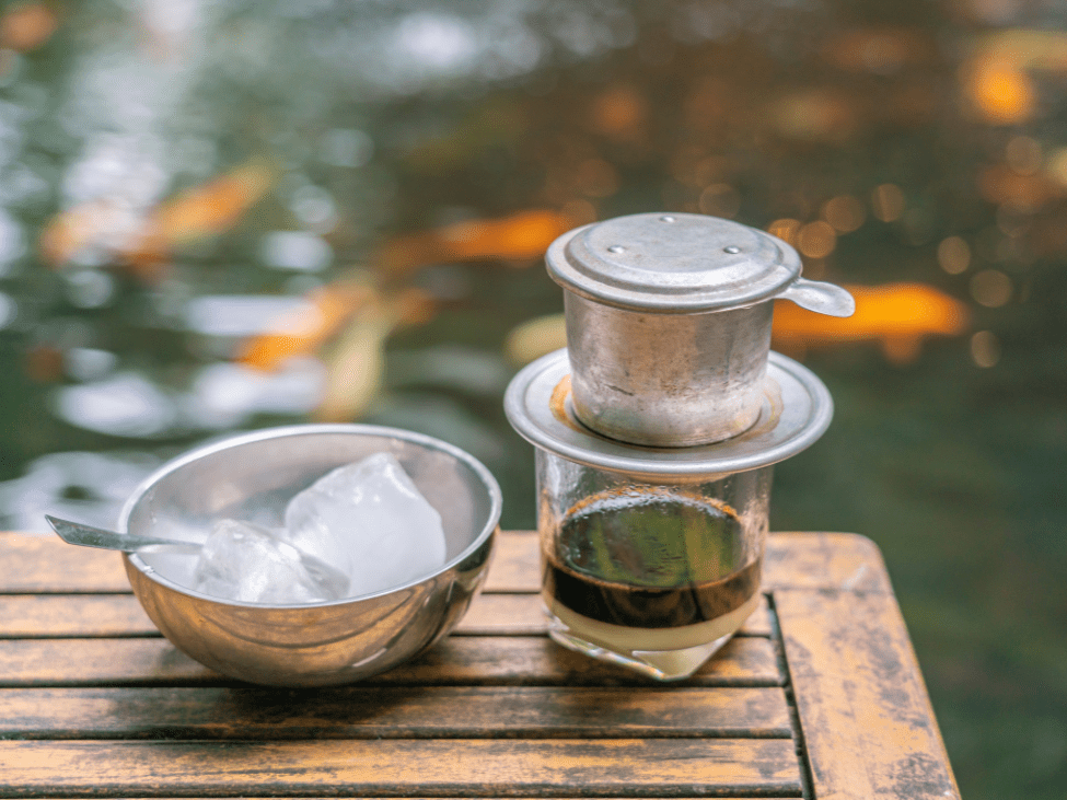 A glass of iced Vietnamese coffee with condensed milk, served on a wooden table with a side of condensed milk.