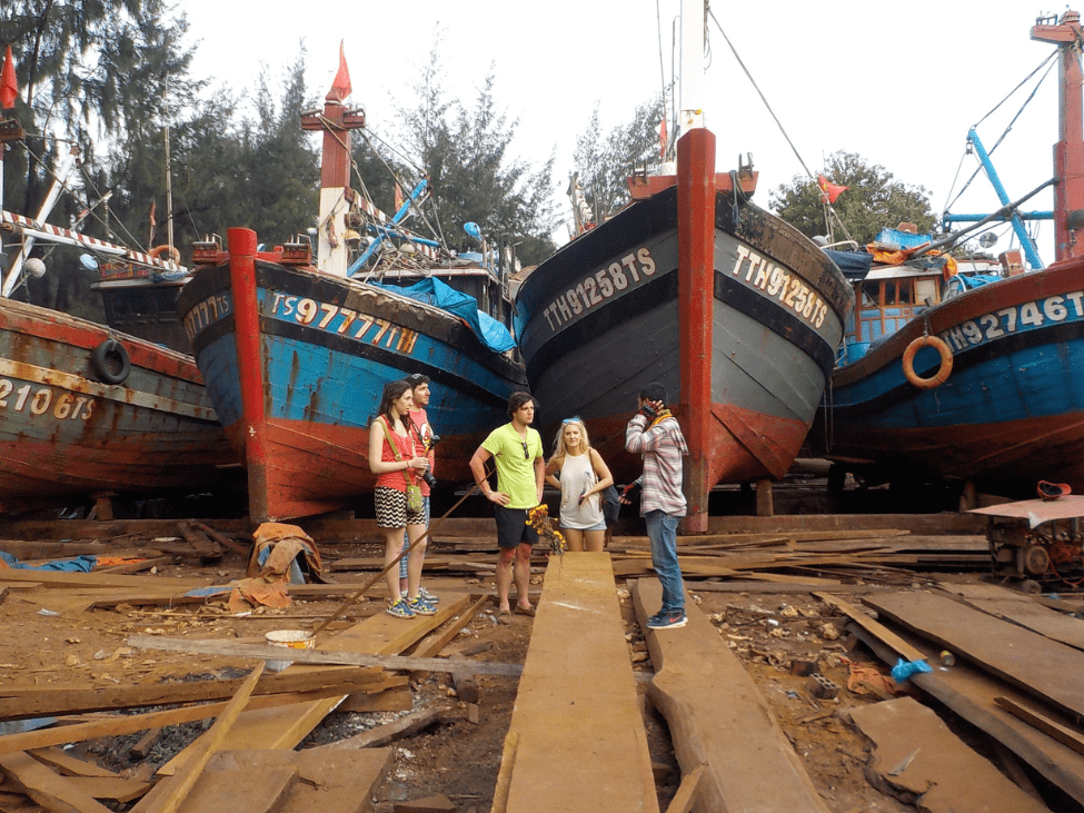 Skilled craftsmen carving a traditional wooden boat at a boat-building yard on Cam Kim Island.