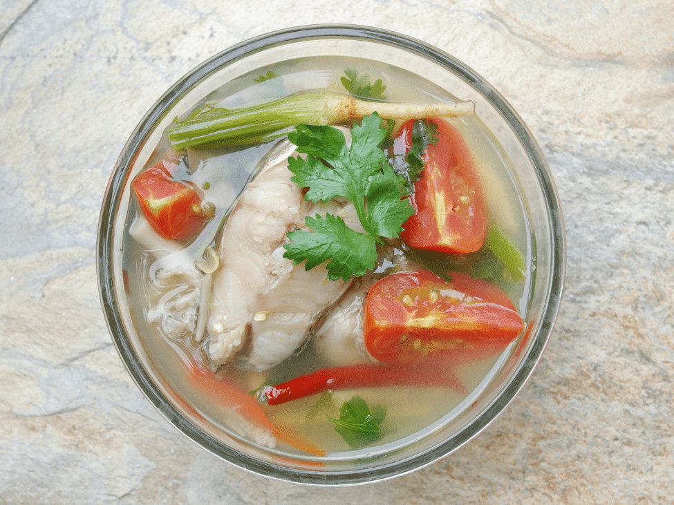 A bowl of Canh Chua with fish, tomatoes, and pineapple in a tamarind broth.