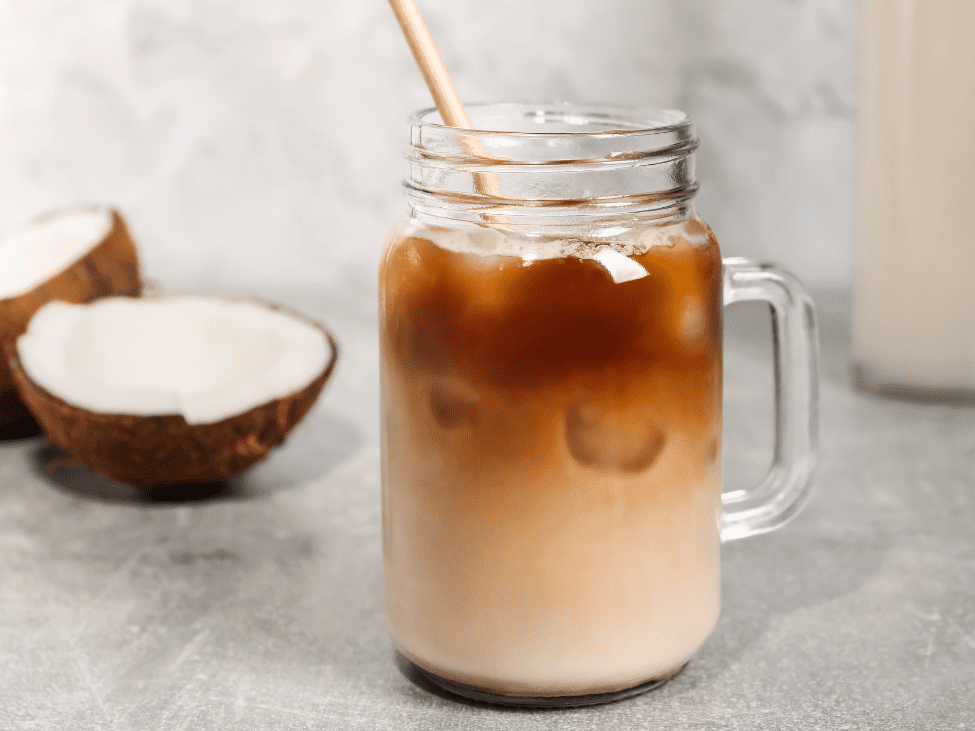 A coconut coffee served in a glass with a topping of whipped cream and a coconut slice as garnish.