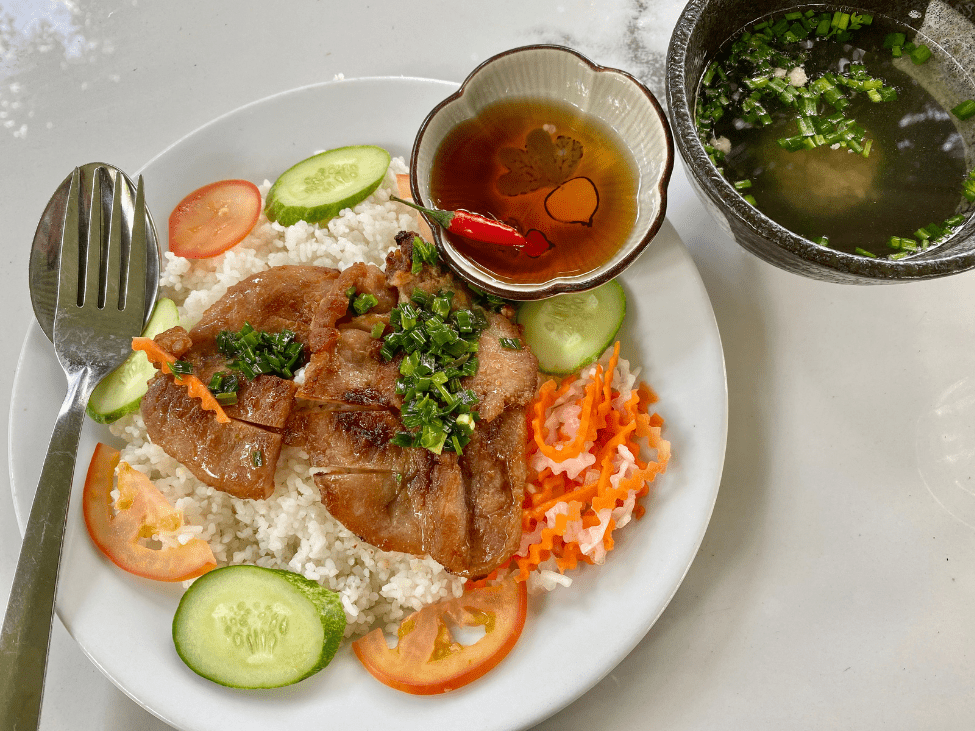 A plate of Cơm Tấm (broken rice) with grilled pork and vegetables.