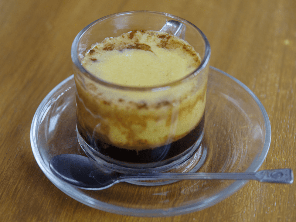 A cup of creamy egg coffee served in a ceramic mug, with a frothy top and a spoon on the side.