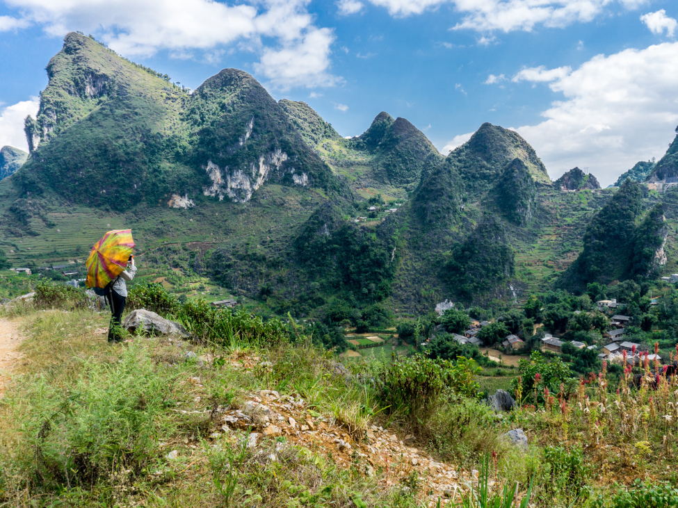 A group of trekkers walking through the mountainous terrain of Ha Giang with local ethnic village in the background.