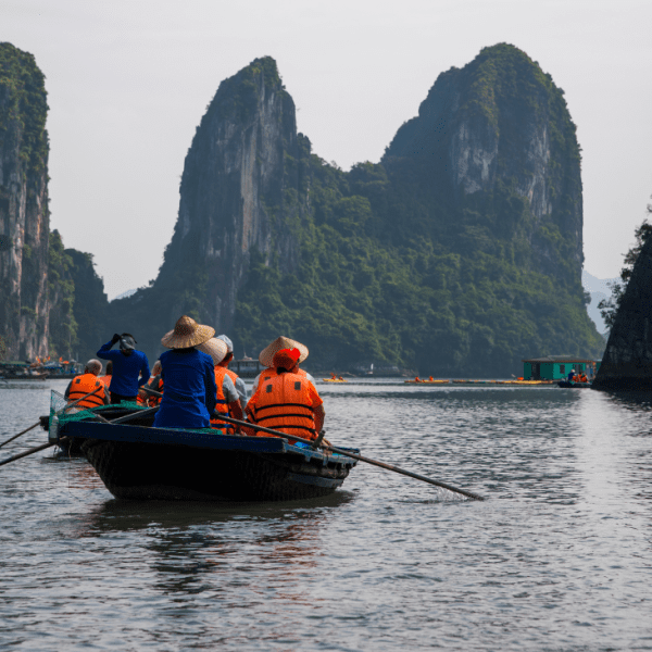 Traditional junk boat sailing through the emerald waters of Ha Long Bay, with limestone karsts in the background.