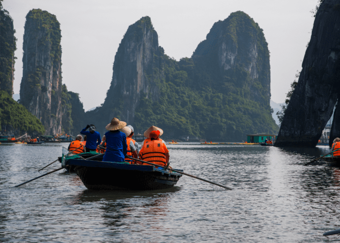 Traditional junk boat sailing through the emerald waters of Ha Long Bay, with limestone karsts in the background.