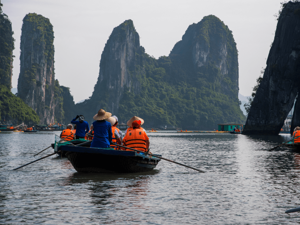 Traditional junk boat sailing through the emerald waters of Ha Long Bay, with limestone karsts in the background.