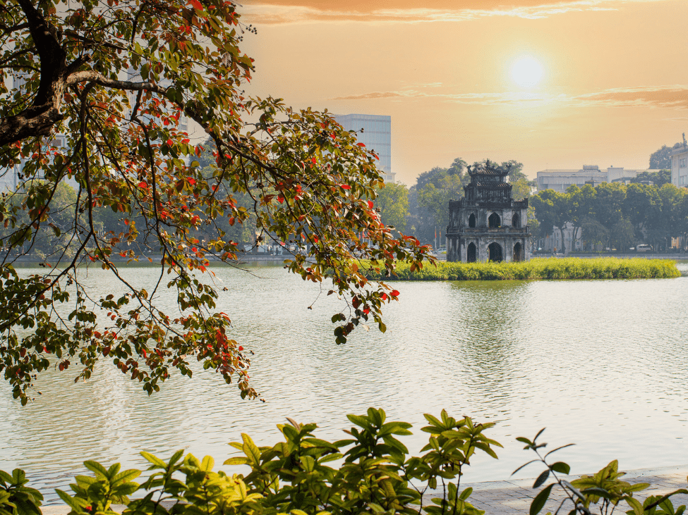 Autumn leaves reflecting on the serene waters of Hoan Kiem Lake in Hanoi.