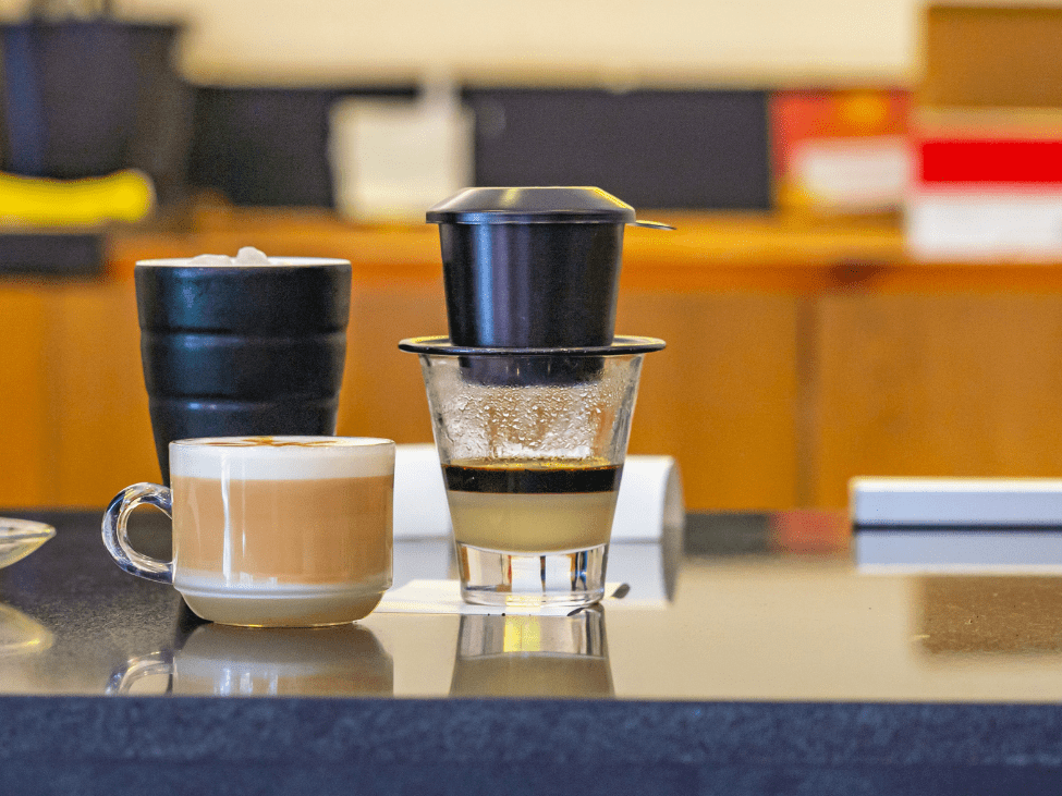 A steaming cup of hot coffee with condensed milk, placed on a saucer with a side of condensed milk.