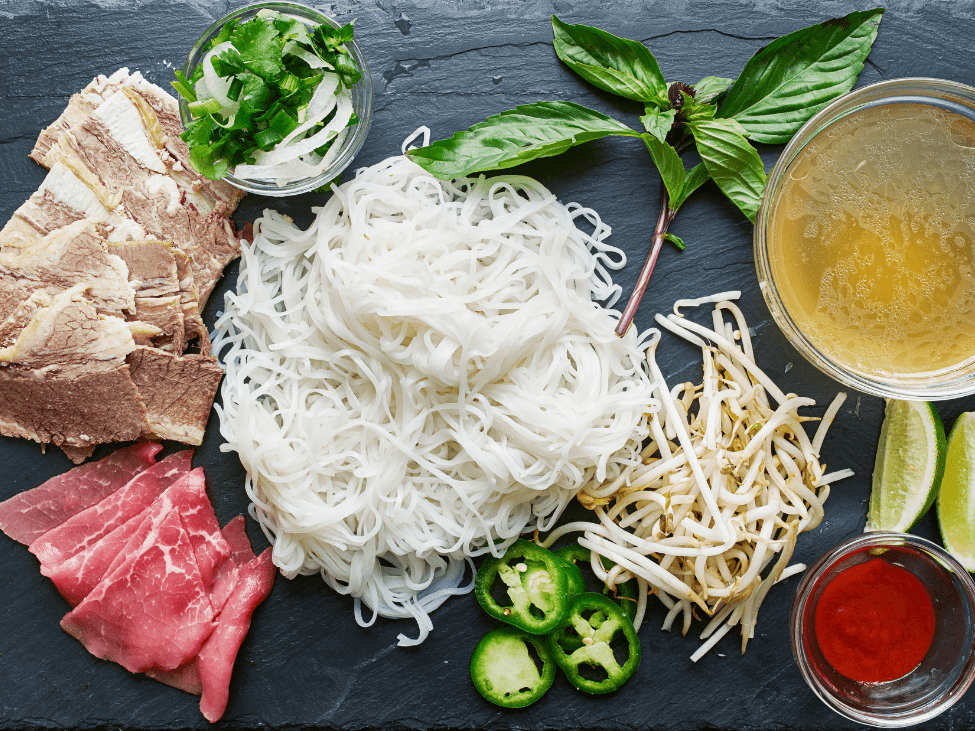 Ingredients for beef pho, including beef bones, star anise, cinnamon, and fresh herbs