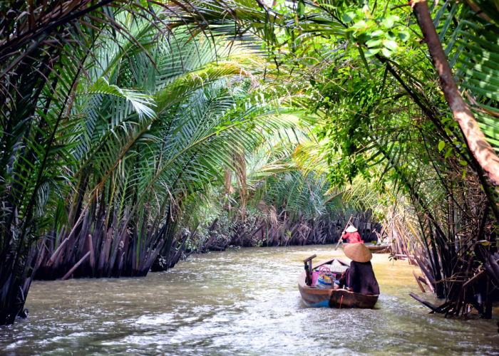 Traditional boat cruising through the Mekong Delta River, surrounded by lush greenery.