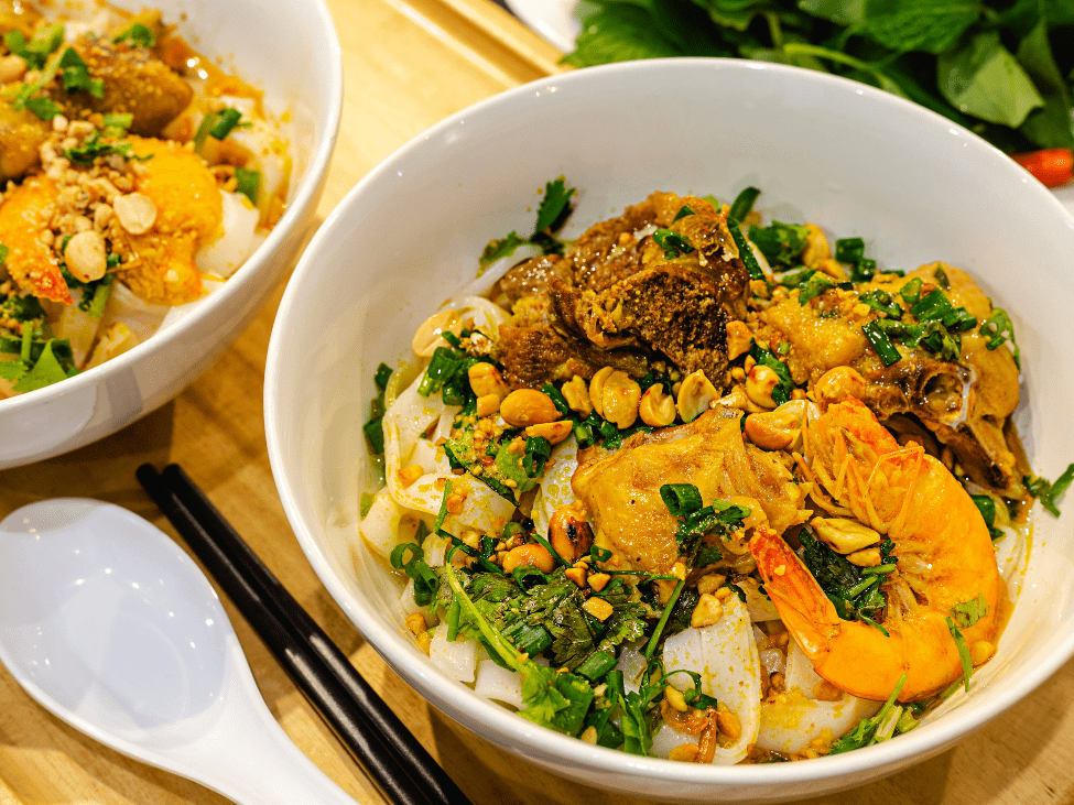 A bowl of Mi Quang with shrimp, pork, herbs, and rice crackers