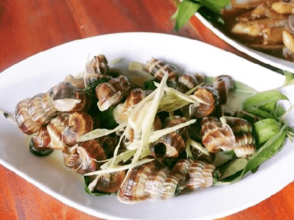 A vibrant dish of snails in coconut milk served at Ốc Chị Em, alongside grilled prawns.